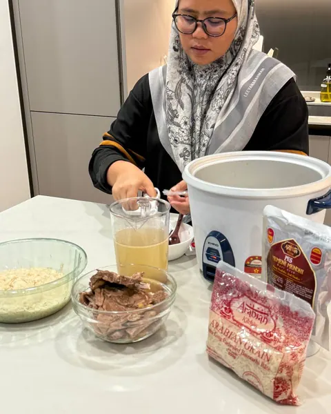 Jug berisi air rebusan daging di sebelah mangkuk beras, daging rebus dan periuk nasi, bersama pek pes Yemeni Mendhi