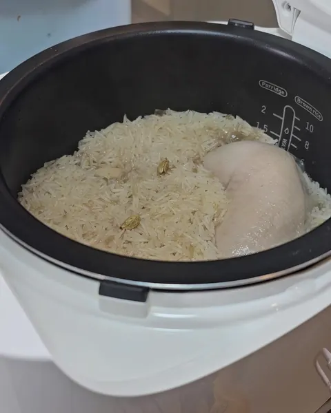 Suku ayam di atas nasi Mendhi yang sudah masak dalam periuk nasi