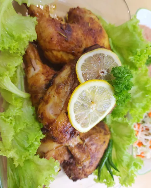 Ayam bakar di atas daun salad dengan hirisan lemon dan daun parsley