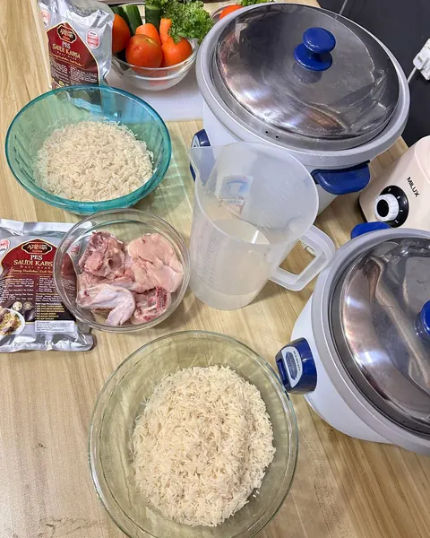 Bahan nasi arab di atas meja: pek pes, beras yang sudah direndam, ayam dan jug air di sebelah periuk nasi