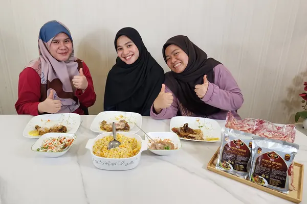 Tiga orang makan nasi arab Yemeni Mendhi bersama di meja, dengan ayam, salatah, sos tomato dan pek pes Arabian Kitchen