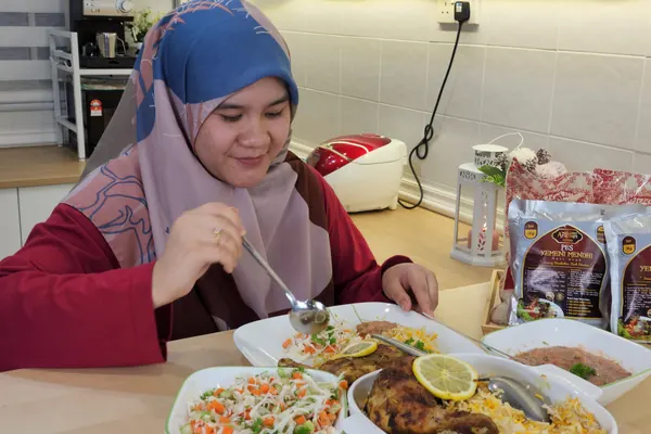 Seorang wanita makan nasi Yemeni Mendhi dengan ayam bakar, salatah dan sos di meja makan, pek pes di sebelah