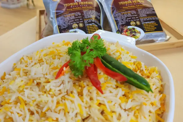 Semangkuk nasi Yemeni Mendhi kuning-putih dengan cili merah, pek pes Arabian Kitchen di belakang