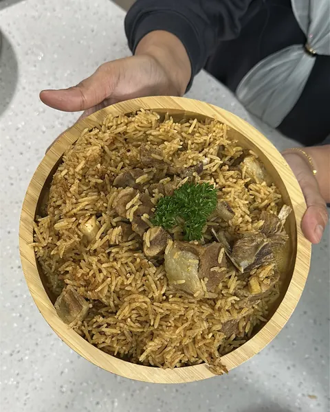 Nasi Kabsa kambing carik dalam mangkuk kayu, dihias daun parsley