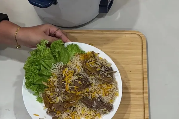 Nasi Yemeni Mendhi kambing di pinggan dengan daun salad, periuk nasi di belakang