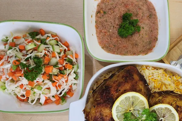 Mangkuk salad sayur dan mangkuk sos tomato bercili di sebelah hidangan nasi arab